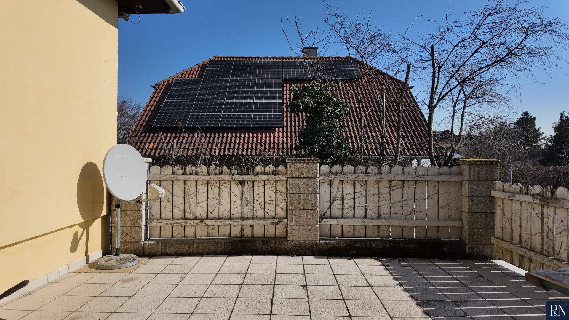 Gedeckte Terrasse mit Fliesenboden und Blick auf ein Nachbarhaus mit Solaranlage.