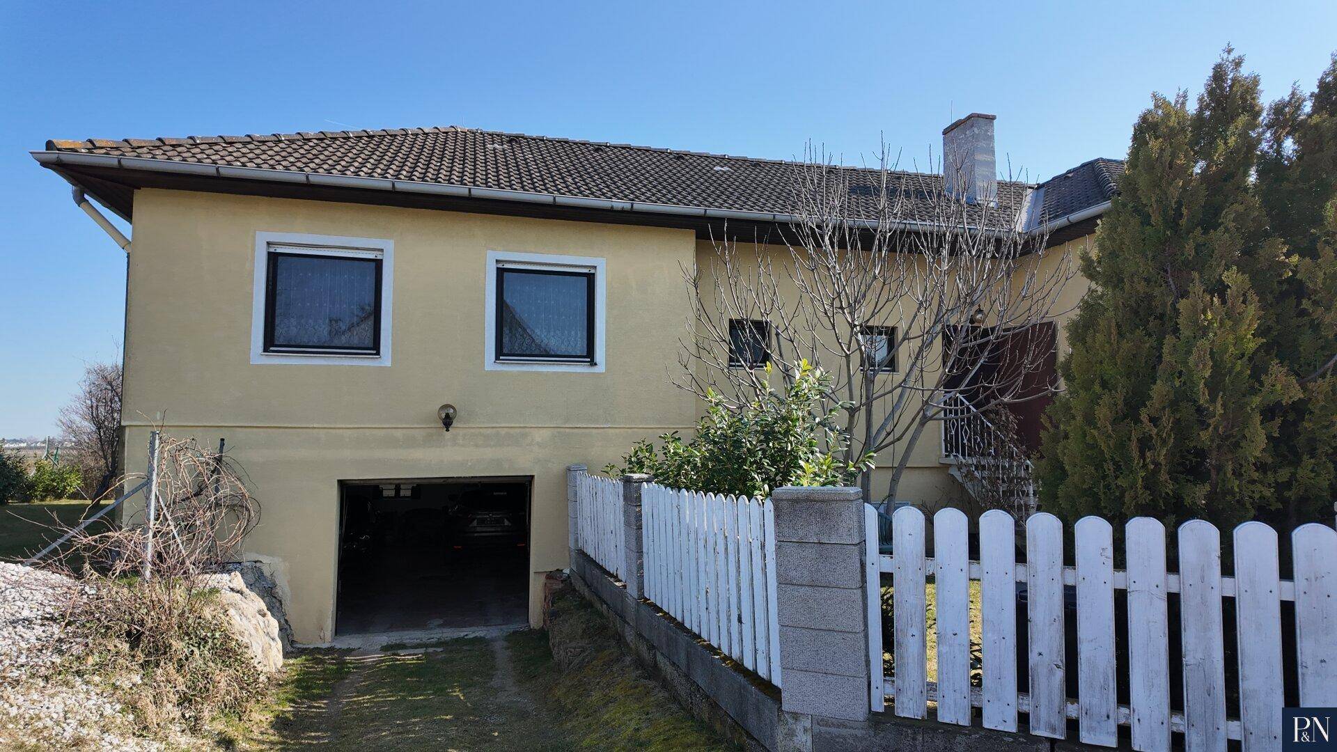 Seitenansicht des Hauses mit Garageneinfahrt und weißem Lattenzaun.