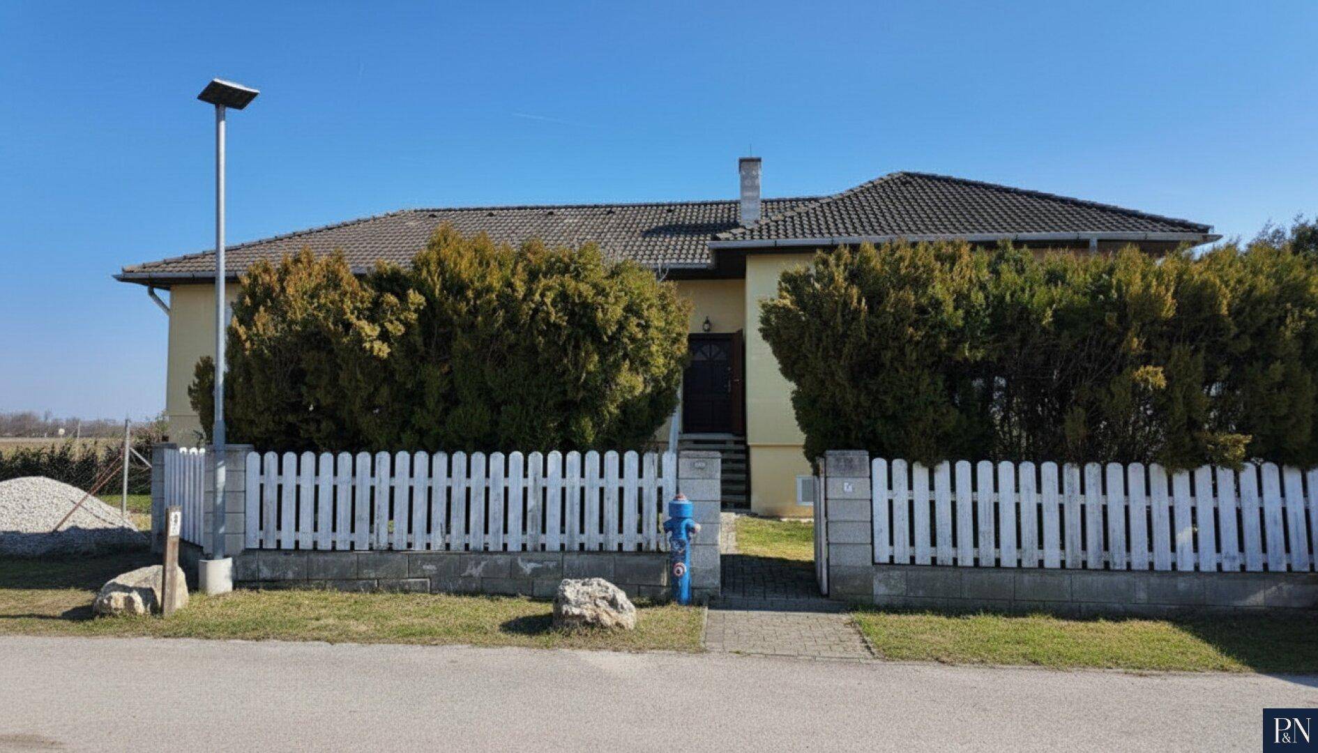 Vorderansicht des Hauses mit gepflegtem Vorgarten und weißem Lattenzaun.