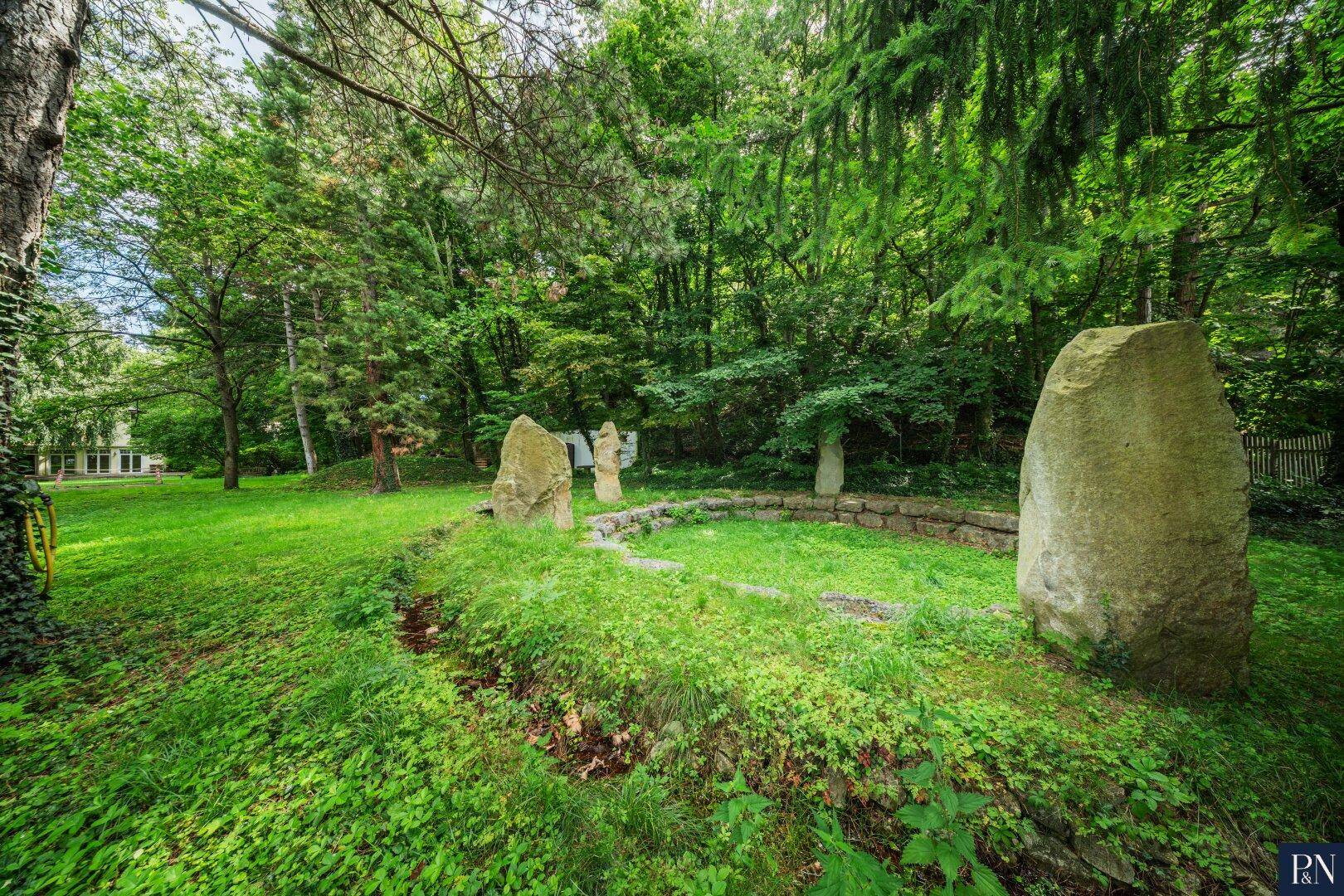 Weitläufiger Gartenbereich mit großen Steinskulpturen und üppiger grüner Vegetation.