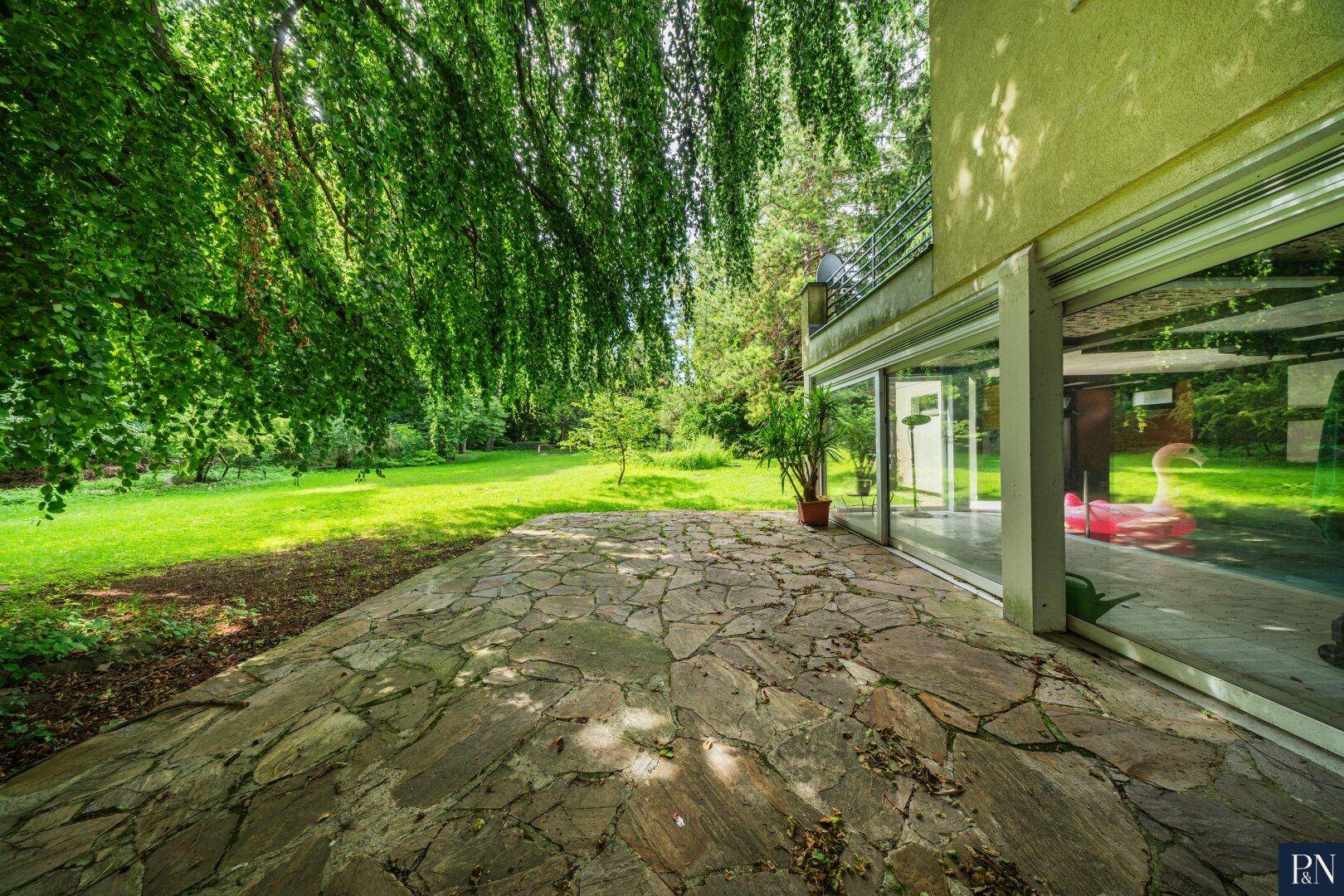 Geräumige Steinterrasse mit Blick auf den Garten und den angrenzenden Innenpool.