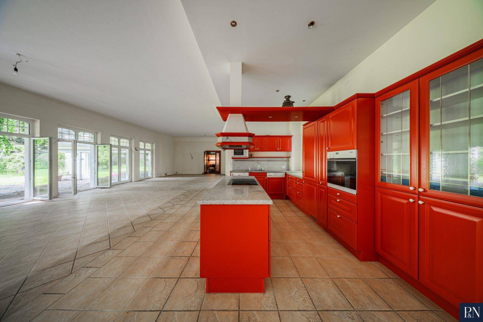 Moderne rote Einbauküche mit Kochinsel, integrierten Geräten und Fliesenboden.