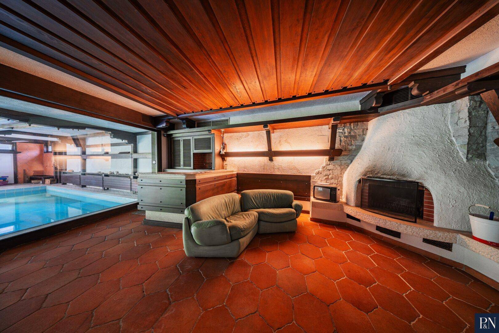 Gemütlicher Wohnbereich mit Kamin, Terrakottafliesen und Blick auf den Innenpool.