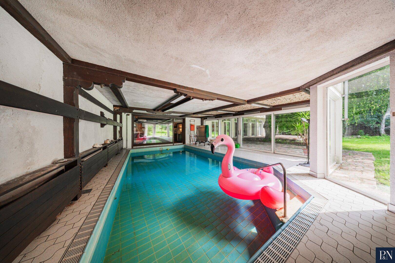 Großzügiger Innenpoolbereich mit Fliesenboden und Blick in den Garten.