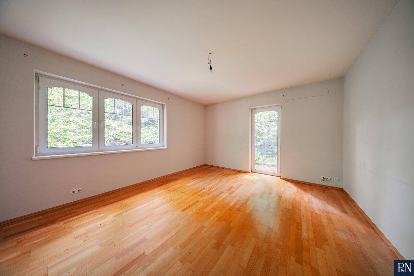 Helles Schlafzimmer mit Holzboden und großen Fenstern mit Blick ins Grüne.