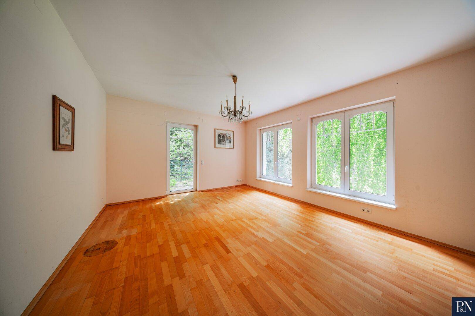 Geräumiges Zimmer mit Holzboden, Kronleuchter und Zugang zum Garten.
