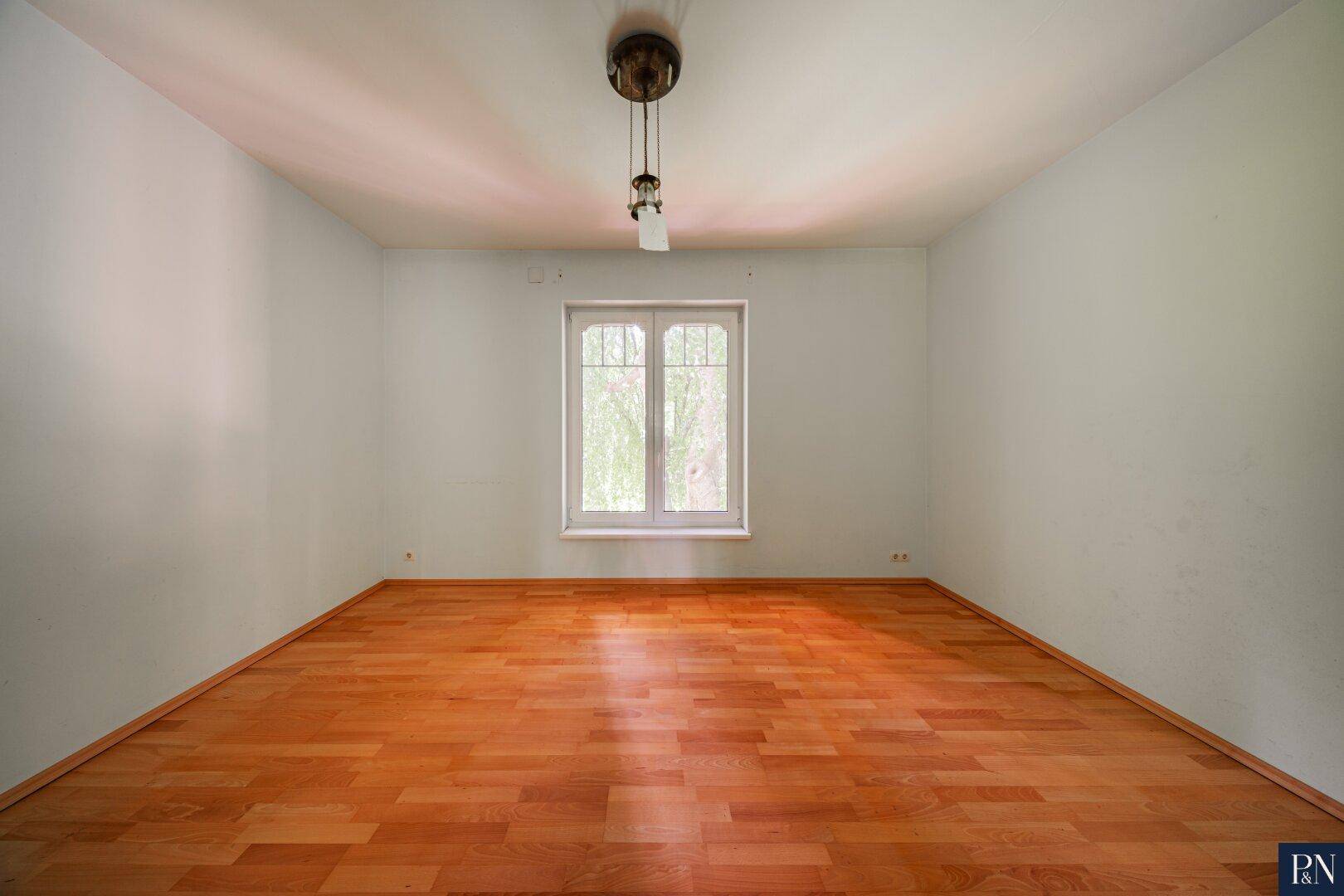 Ruhiges Zimmer mit Holzboden und großem Fenster, ideal als Schlaf- oder Arbeitszimmer.