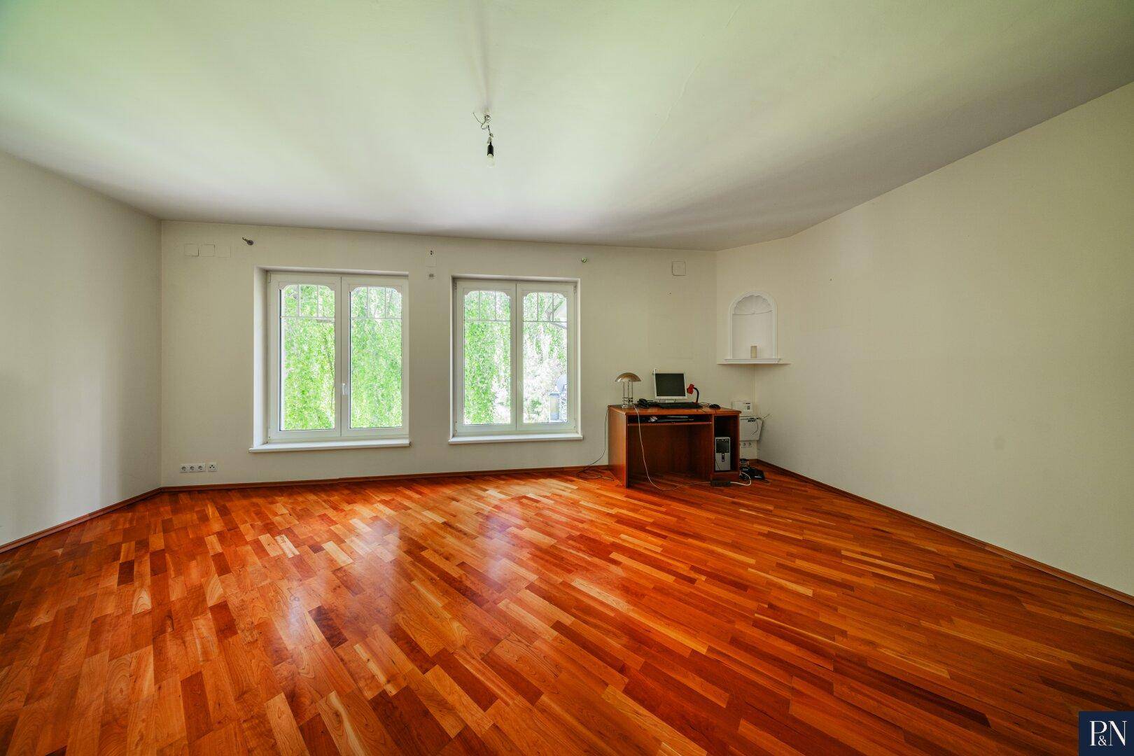 Helles Arbeitszimmer mit Holzboden, zwei Fenstern und einer kleinen Nische.