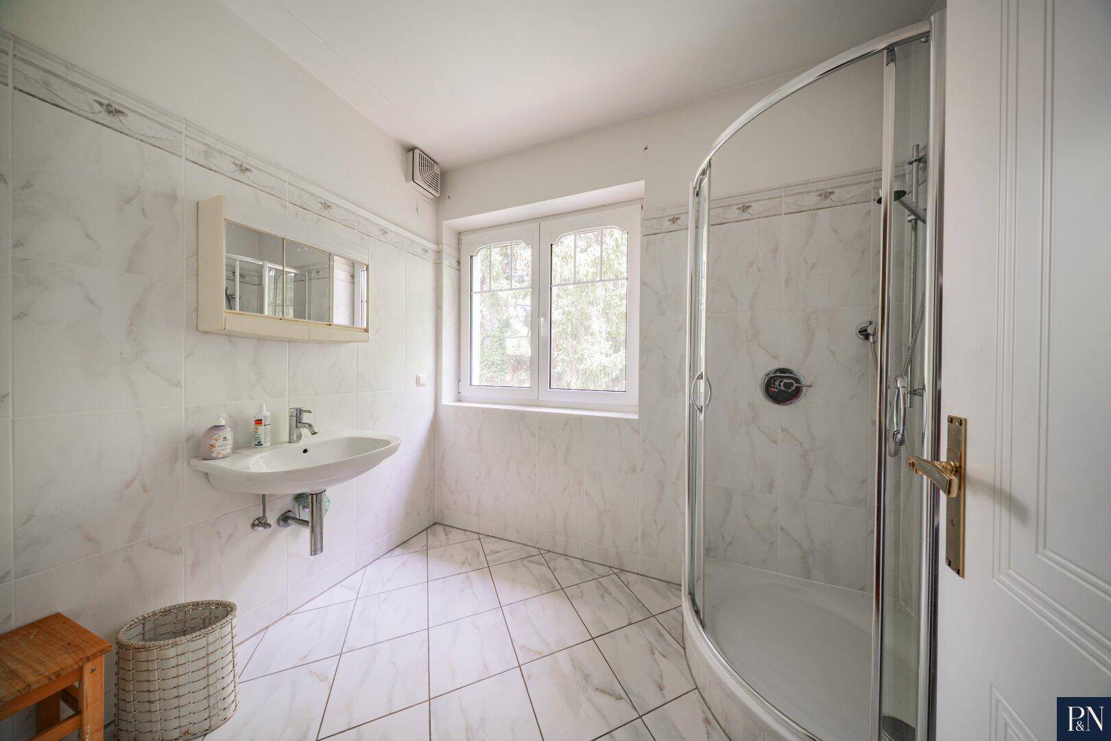 Kleines Badezimmer mit Duschkabine, Waschbecken und Fenster für Tageslicht.