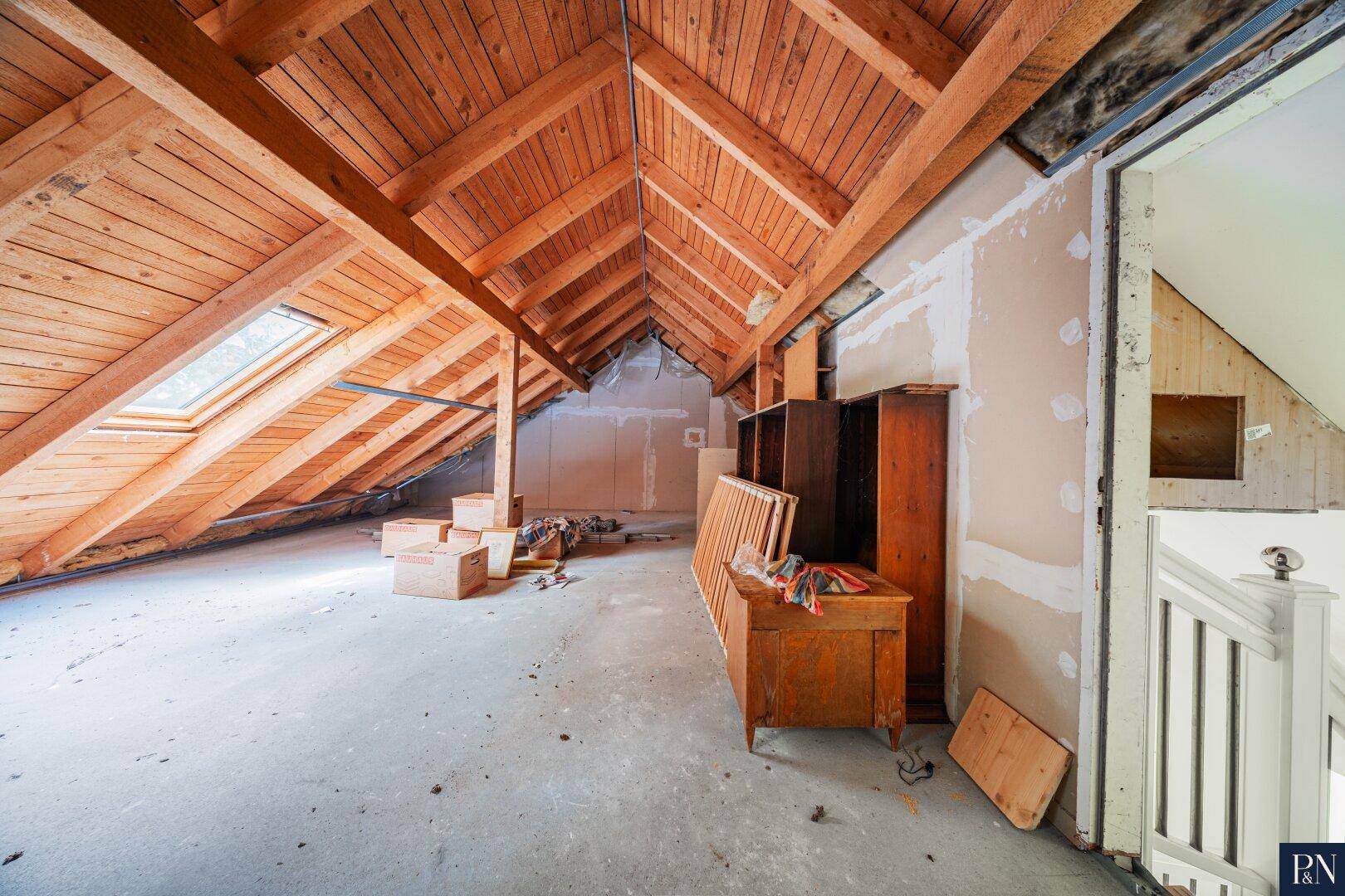 Unausgebauter Dachboden mit sichtbaren Holzbalken und Dachfenstern für Tageslicht.