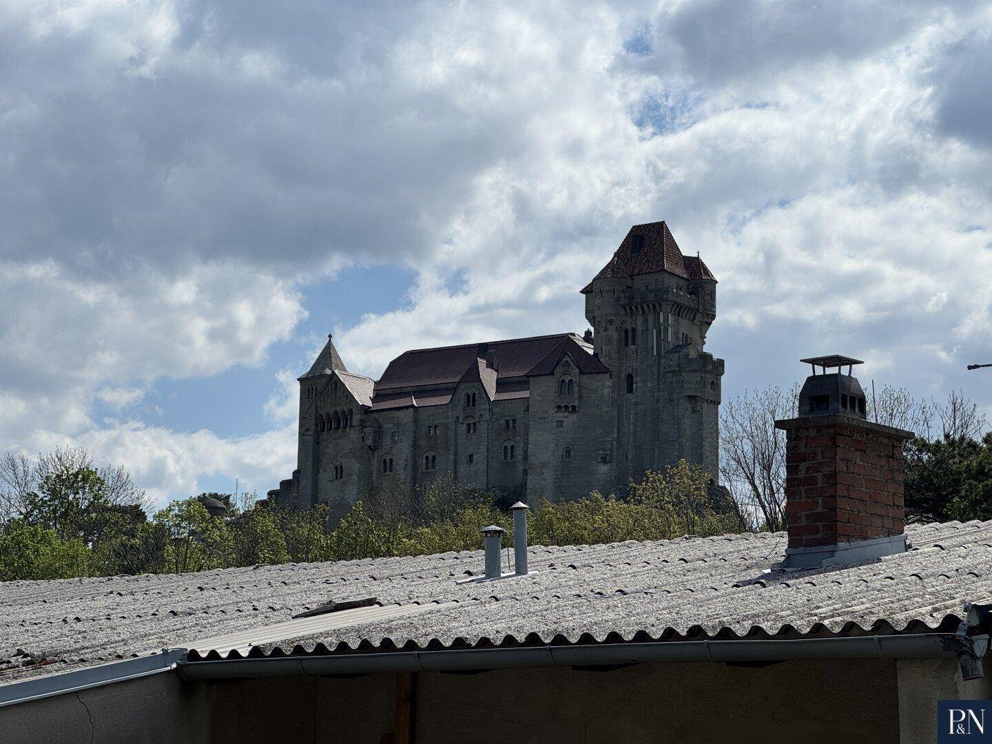 Historisches Schloss auf einem Hügel, sichtbar über einem Dach mit Schornstein.