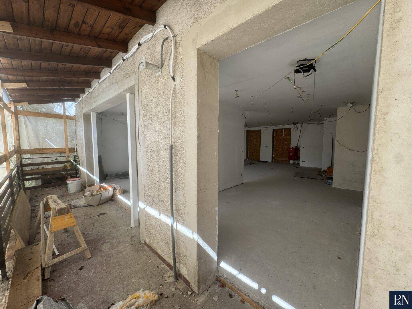 Unfertiger Innenraum mit Zugang zu einem im Bau befindlichen Außenbereich mit Holzbalken.