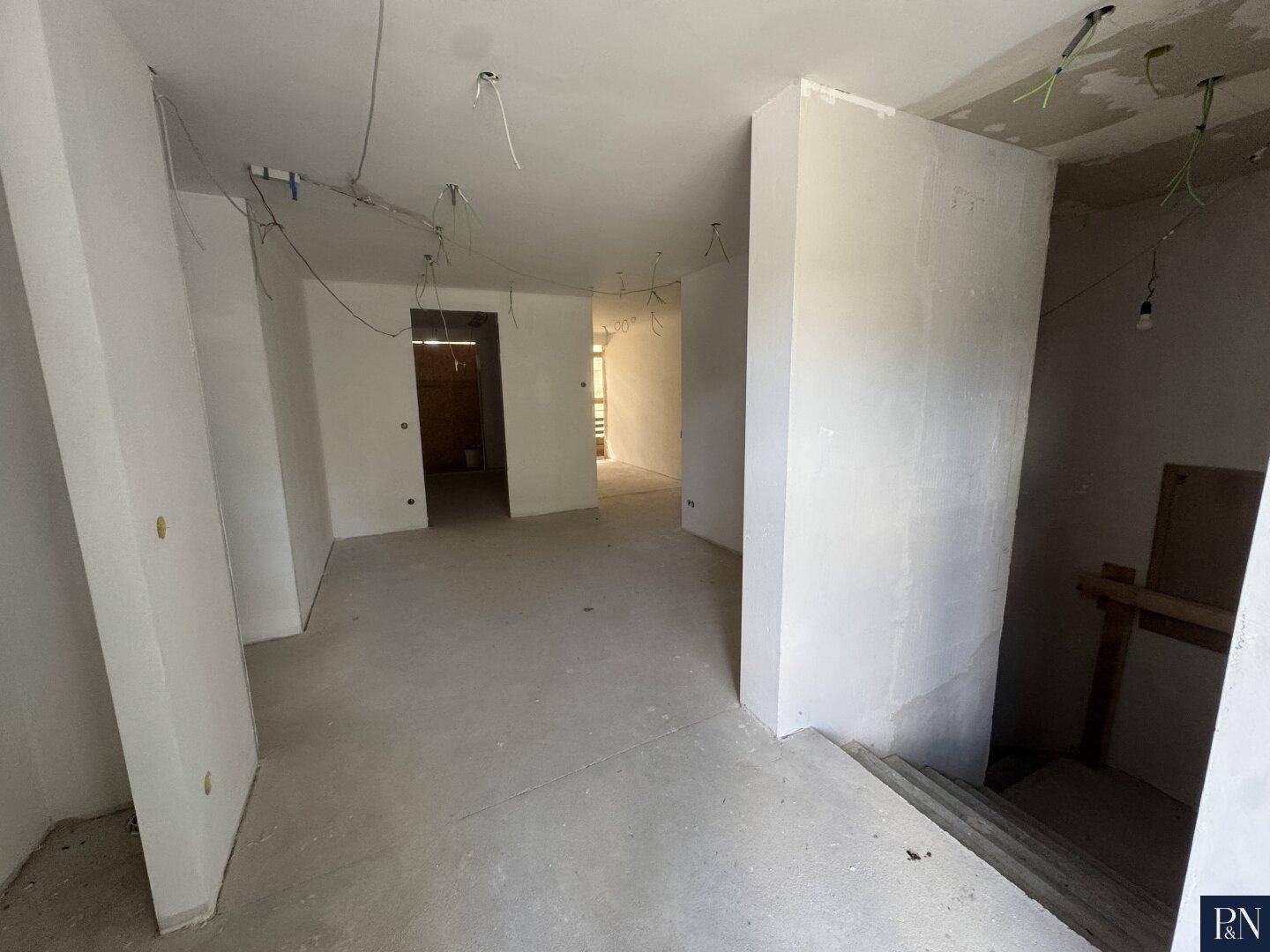 Unfertiger Flurbereich mit Treppenaufgang und sichtbaren Wänden im Rohbauzustand.
