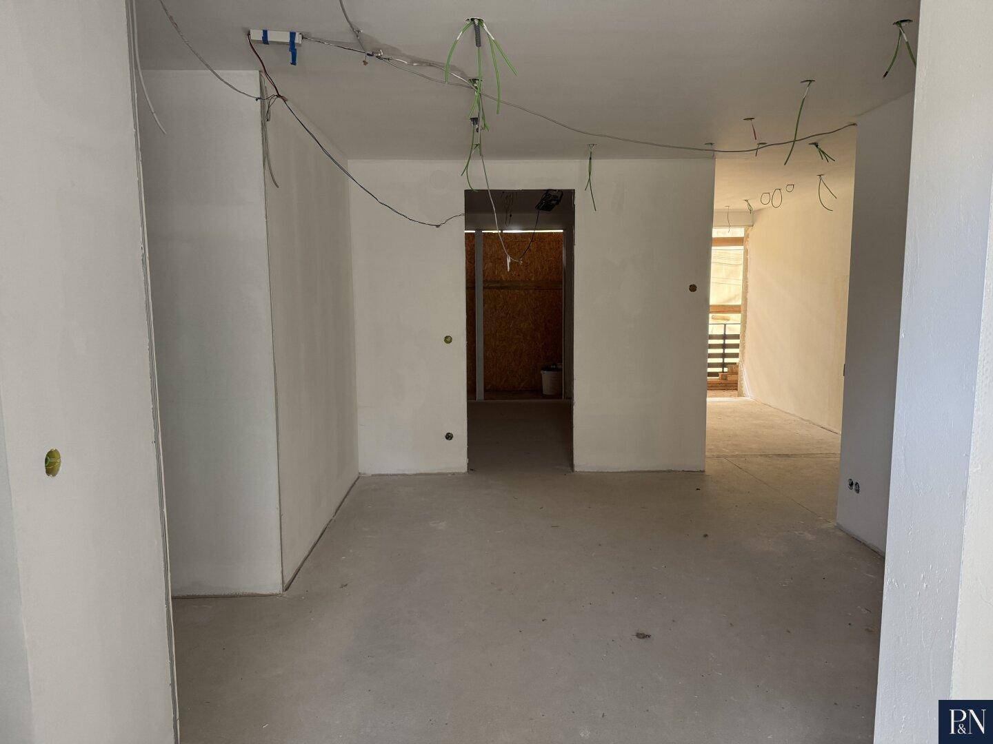 Großer Raum im Rohbau mit vorbereiteten Türöffnungen und Betonboden, bereit für den Ausbau.