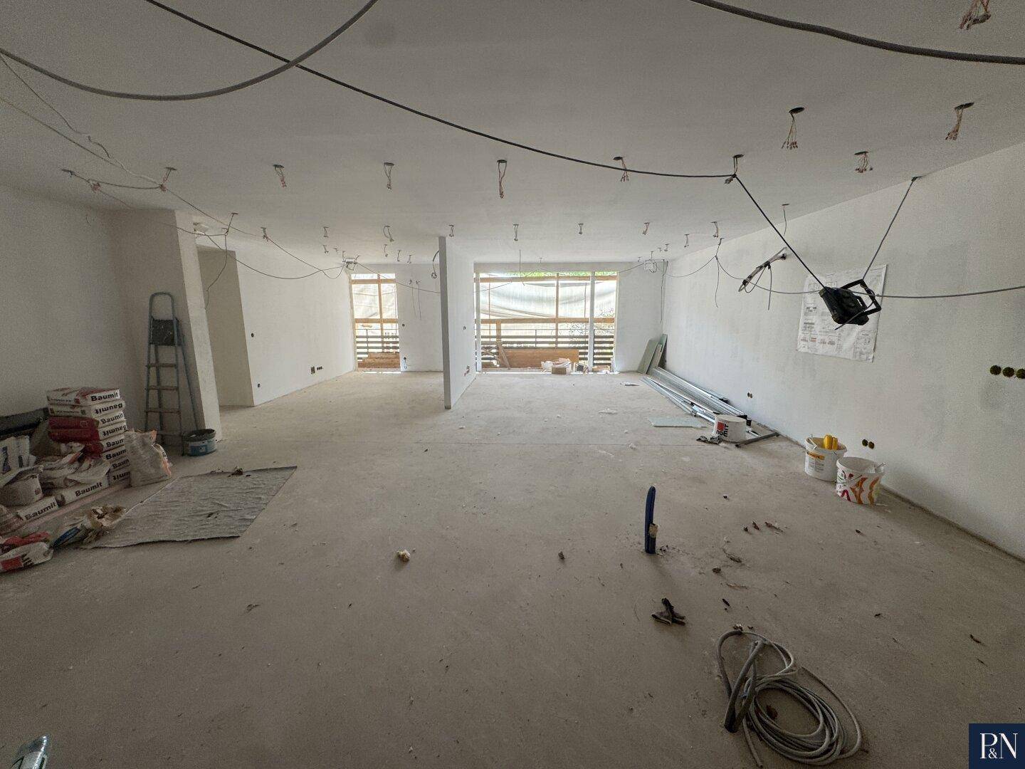 Geräumiger Rohbau mit Betonboden und vorbereiteten Elektroinstallationen für die Beleuchtung.
