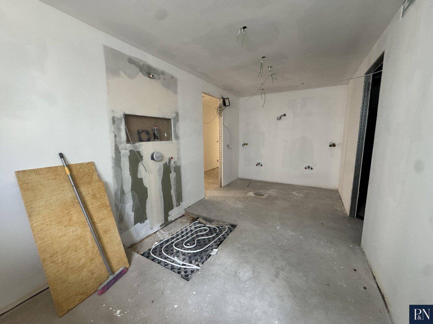 Raum im Rohbau mit sichtbaren Rohren der Fußbodenheizung und vorbereiteten Wänden.
