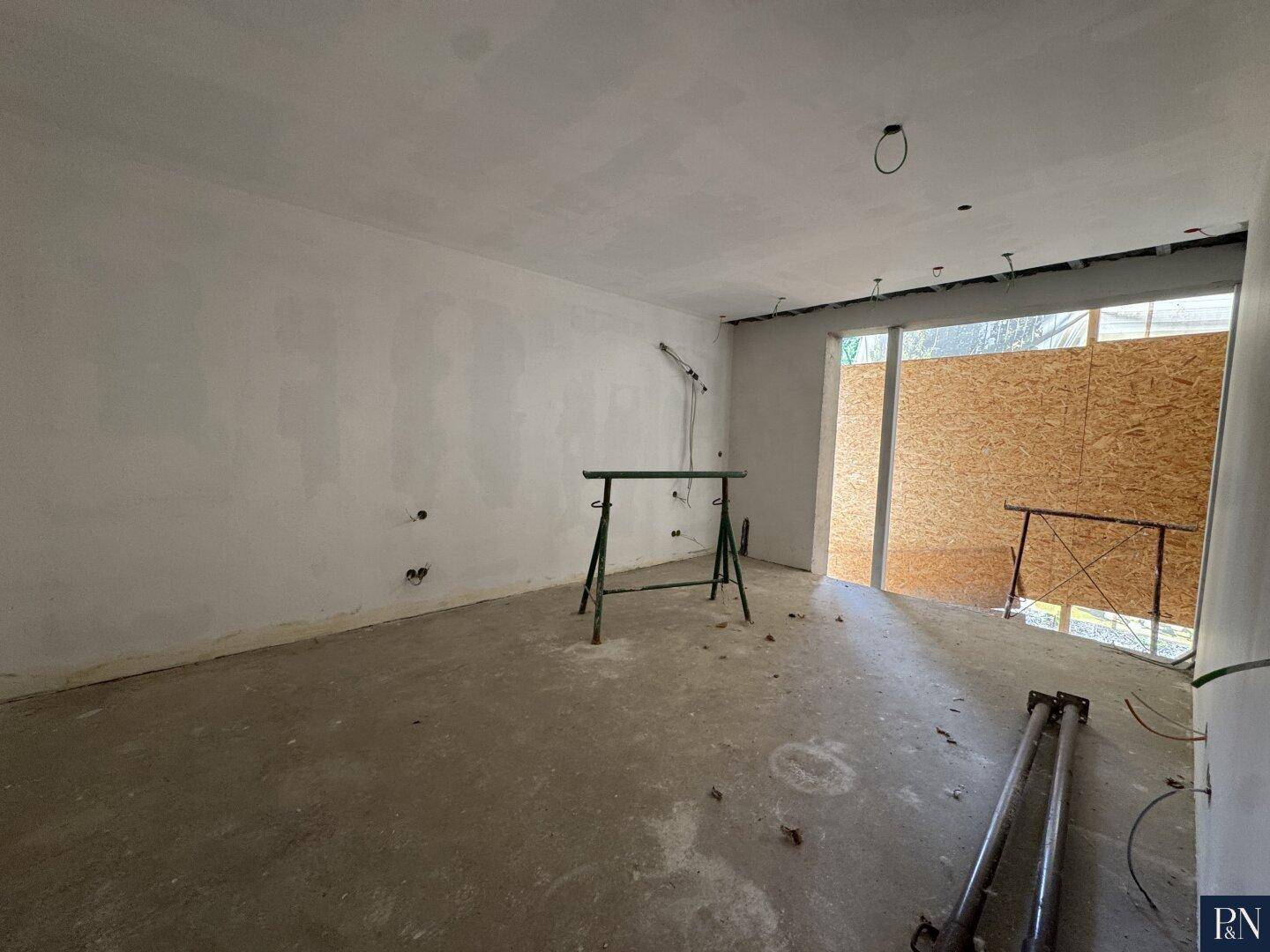 Großer Raum im Rohbau mit breiter Öffnung nach außen, bereit für Fenster oder Türen.