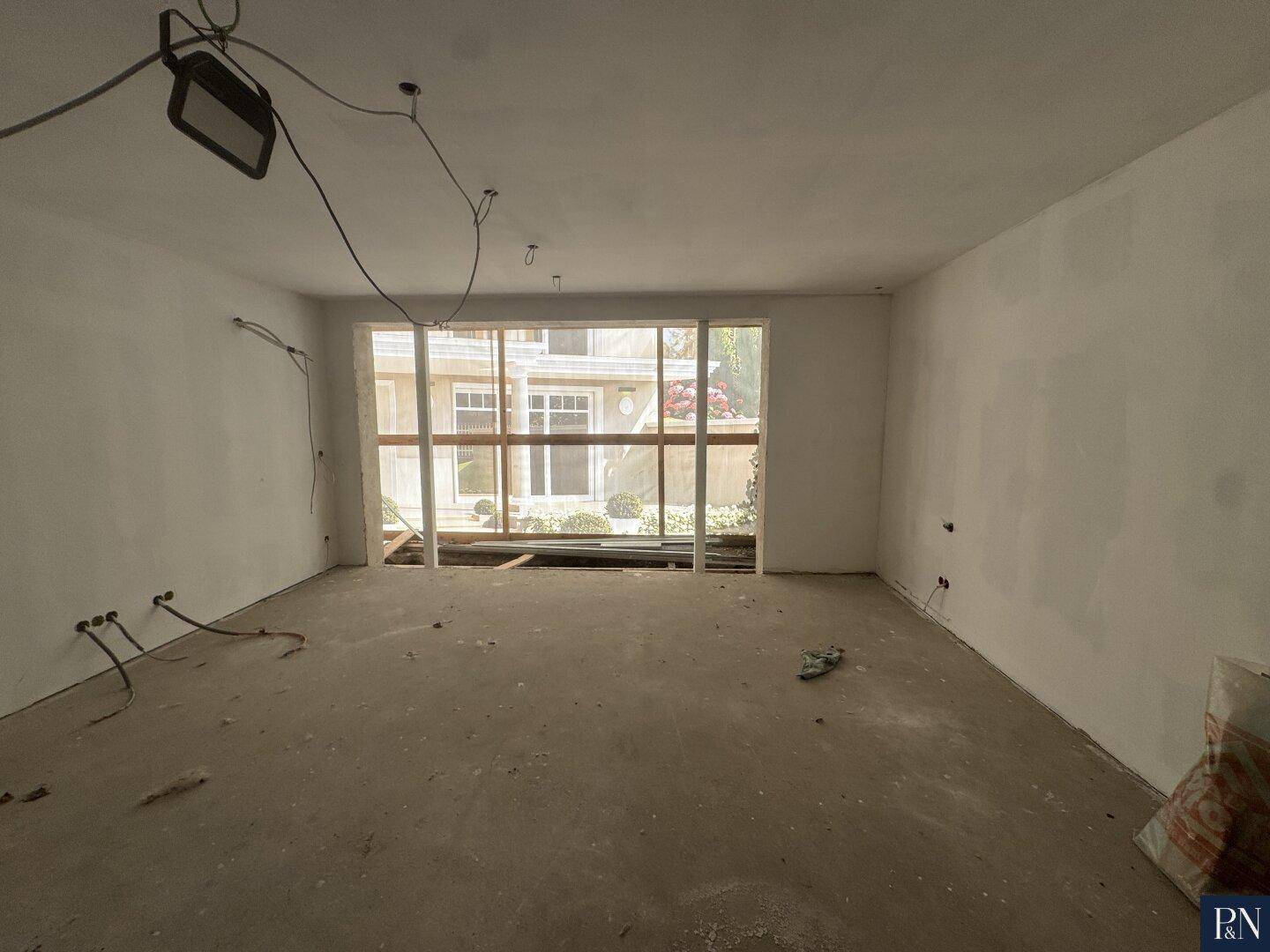 Unfertiger Raum mit großen Fensteröffnungen, die einen Blick auf das Äußere des Gebäudes ermöglichen.