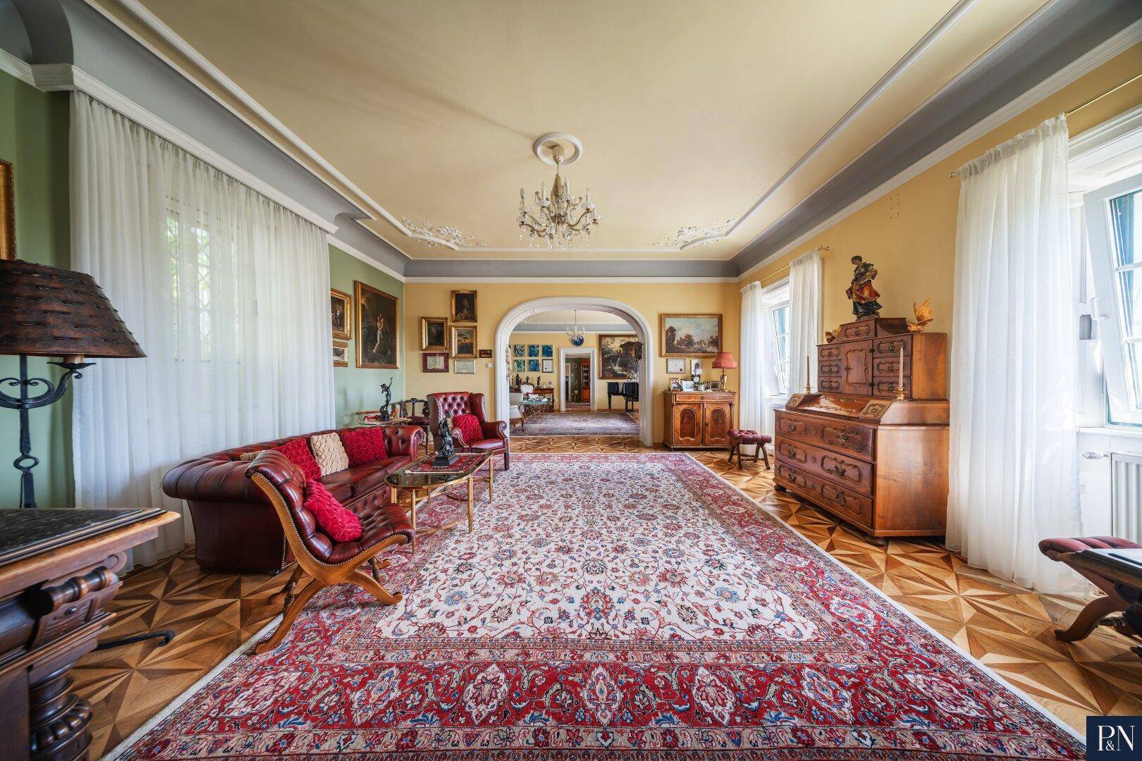 Geräumiges Wohnzimmer mit klassischem Interieur, Parkettboden und Blick in angrenzende Räume.