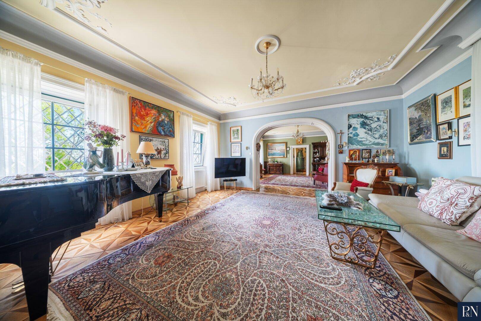 Elegantes Wohnzimmer mit Parkettboden, Flügel und Stuckdecke, offen zu weiteren Räumen.