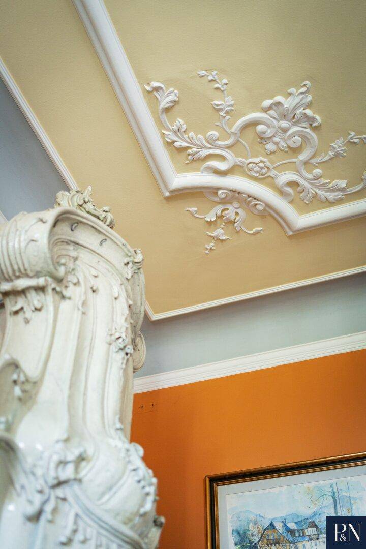Detailaufnahme einer kunstvollen Stuckdecke und eines historischen Kachelofens in einem eleganten Raum.