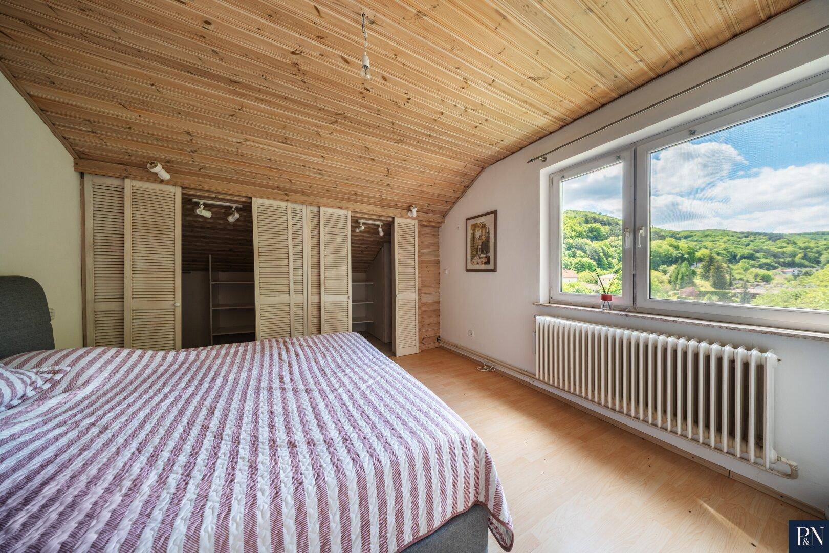 Schlafzimmer im Dachgeschoss mit Holzverkleidung, Dachschräge und weitem Ausblick.