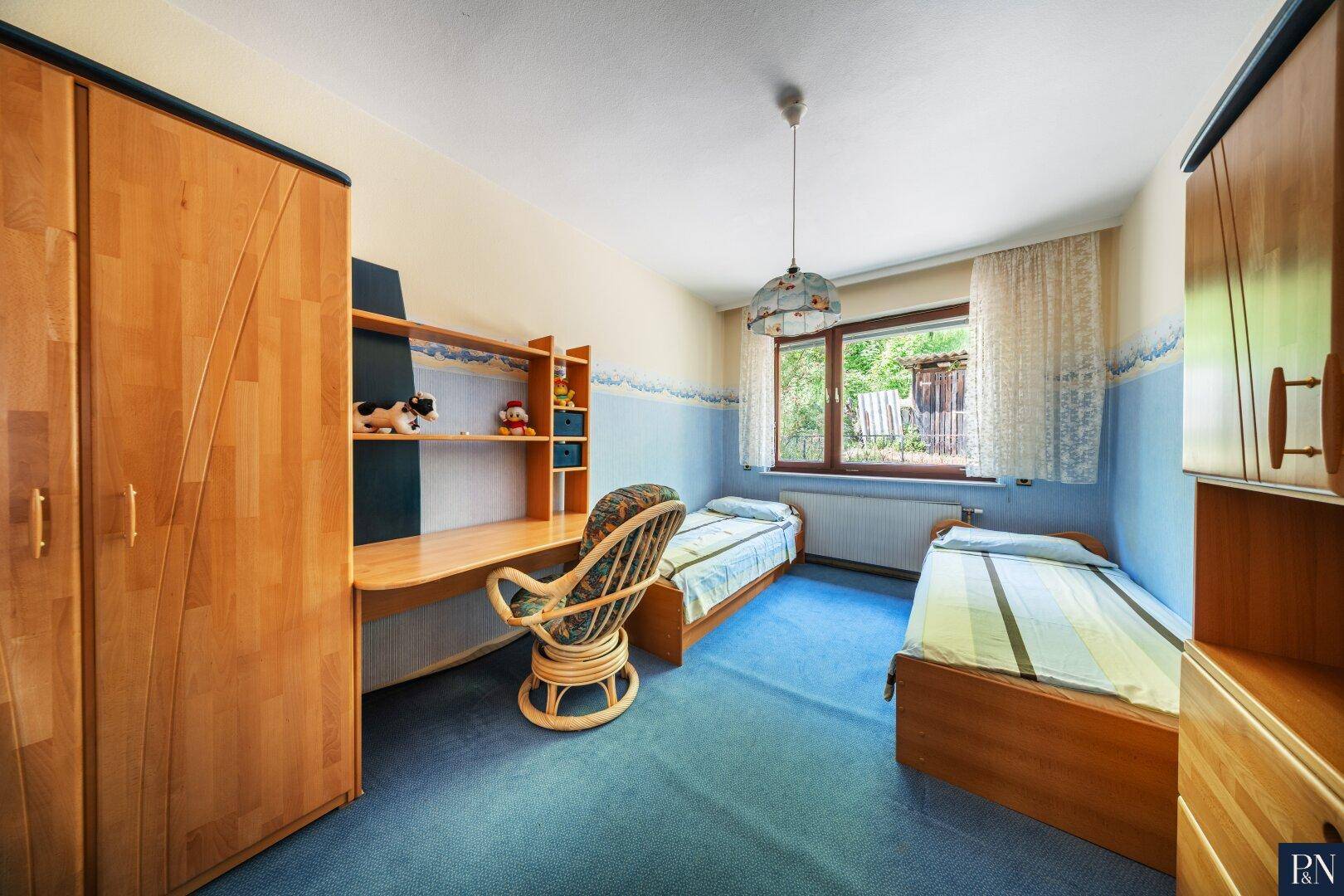 Kinderzimmer mit zwei Einzelbetten, Schreibtisch und blau-weißer Wandgestaltung.