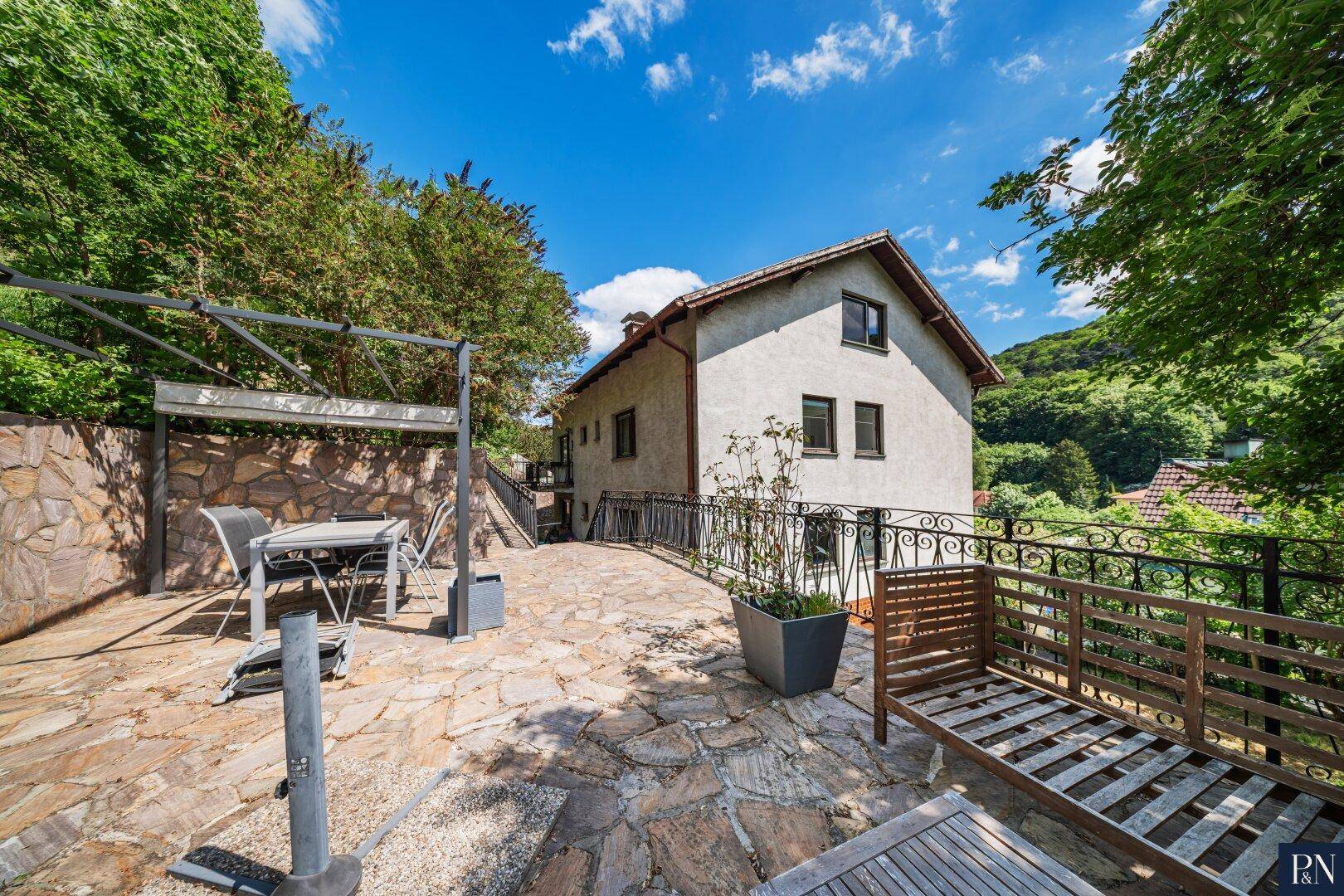 Weitläufige Steinterrasse mit Sitzgelegenheiten und Blick auf das Haus und die Natur.
