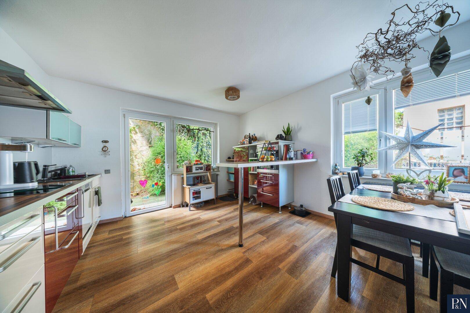 Helle Küche mit Holzboden, weißer Einbauküche und Zugang zum Gartenbereich.
