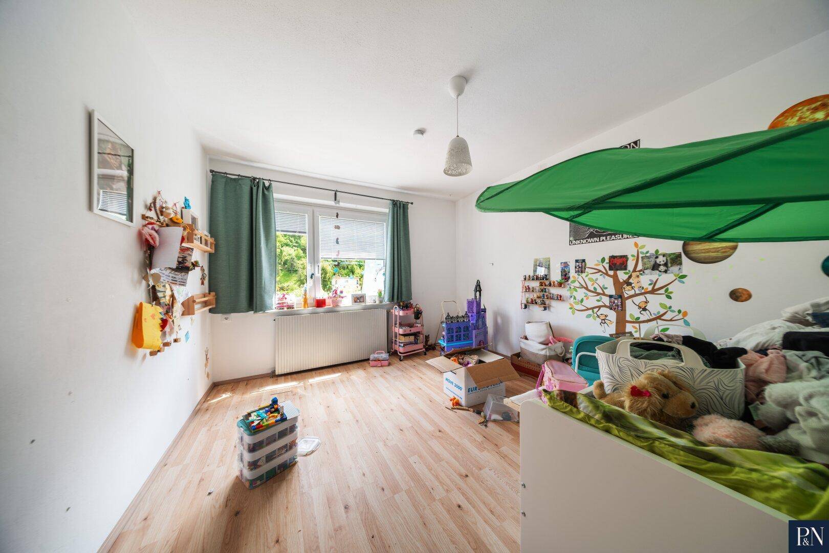 Kinderzimmer mit Holzboden, hellem Anstrich und Blick ins Grüne durch das Fenster.