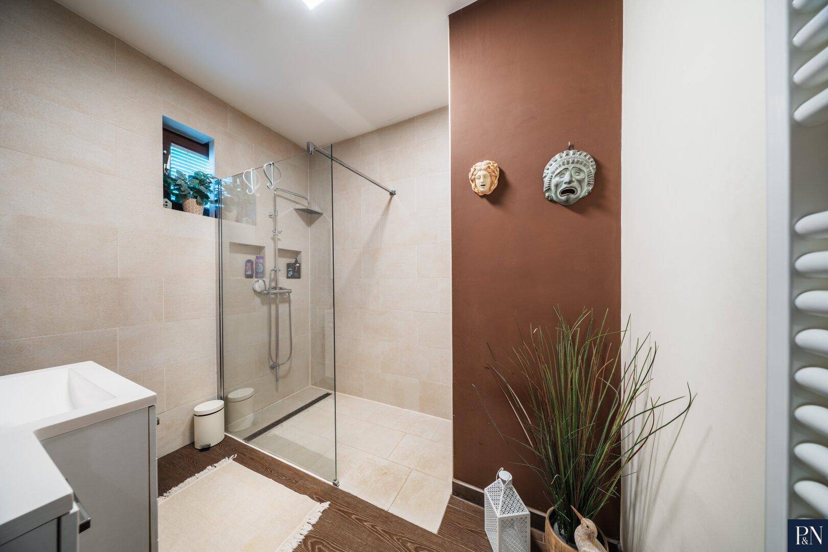 Modernes Badezimmer mit begehbarer Dusche, beigefarbenen Fliesen und einem kleinen Fenster.