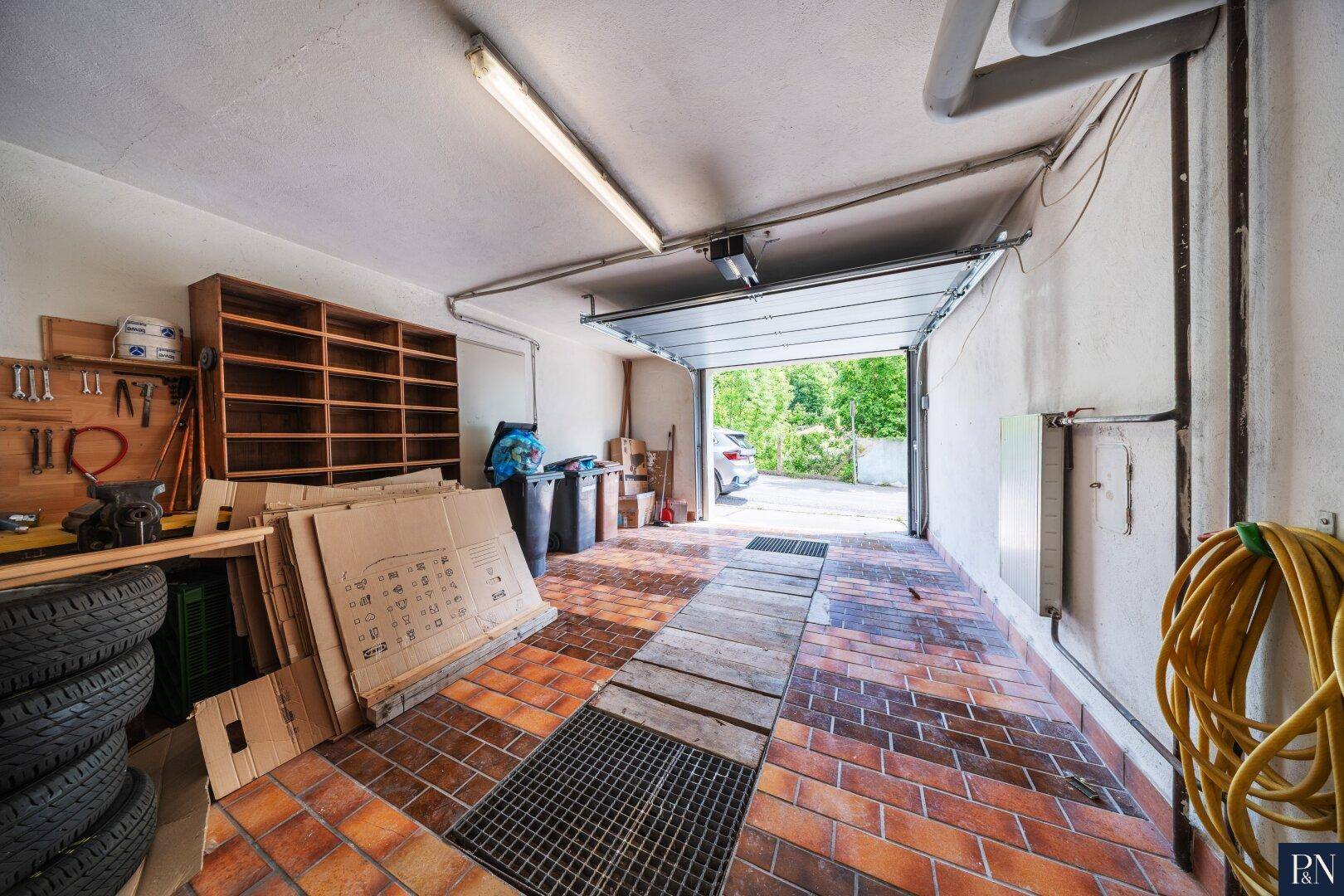 Geräumige Garage mit Fliesenboden, Werkbank und direktem Zugang nach draußen.