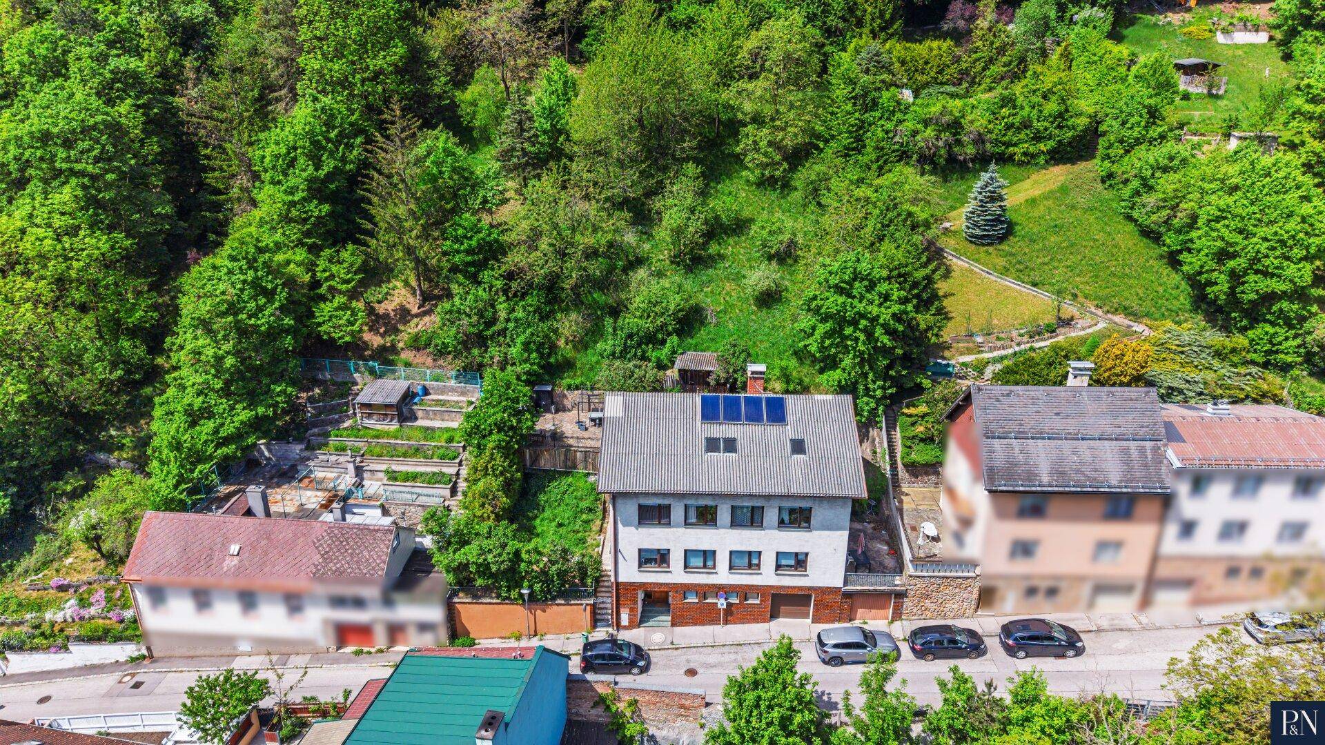Luftaufnahme des Hauses mit Solaranlage auf dem Dach und umgebender grüner Hügellandschaft.
