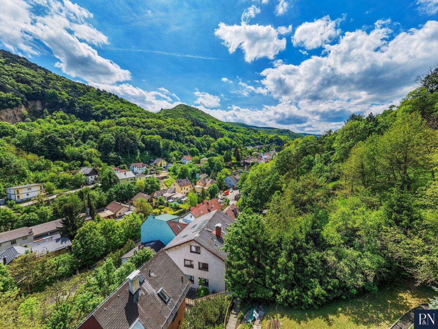Panoramablick auf die grüne Hügellandschaft und die umliegende Wohnsiedlung unter blauem Himmel.