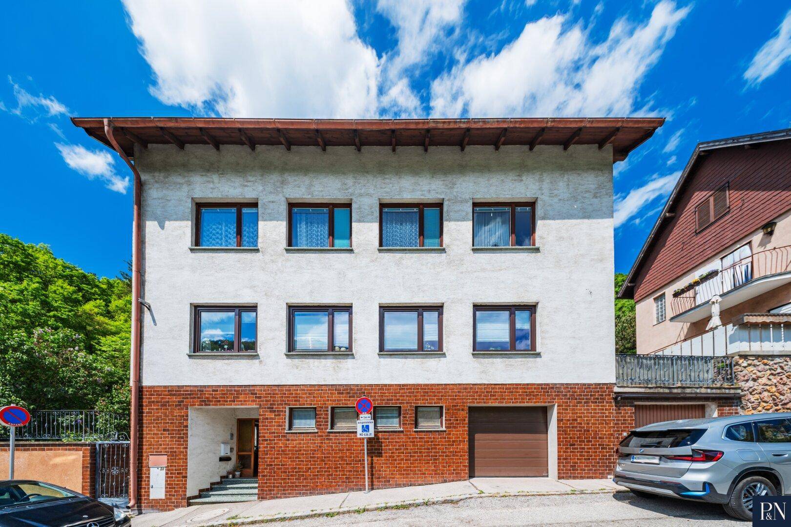 Mehrfamilienhaus mit weißer Fassade, roten Ziegeln und integrierter Garage unter blauem Himmel.