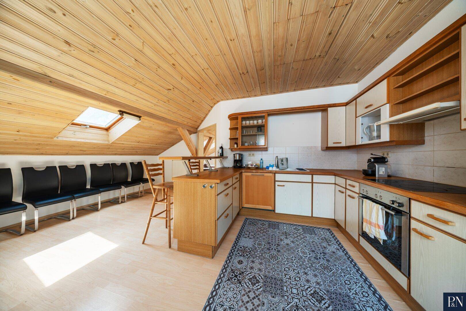 Dachgeschossküche mit Holzverkleidung, Dachfenstern und integriertem Essbereich.