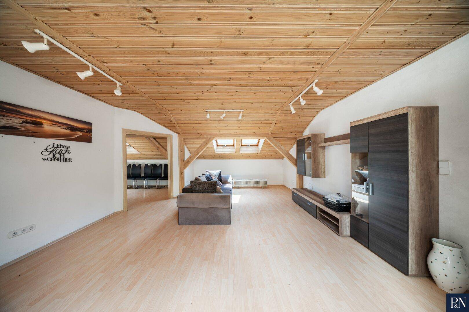 Geräumiges Wohnzimmer im Dachgeschoss mit Holzdecke, Dachfenstern und hellem Holzboden.
