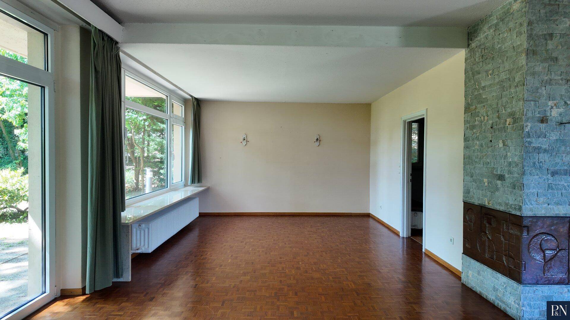 Helles Wohnzimmer mit großen Fenstern, die viel Tageslicht hereinlassen, und einem Steinkamin.