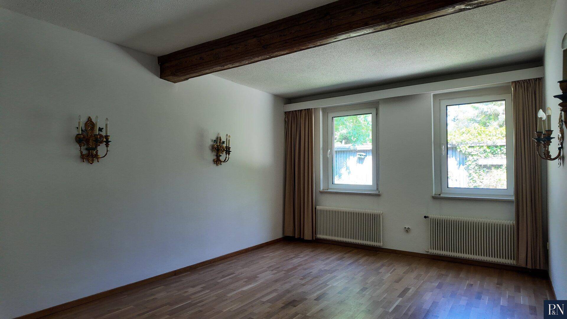 Schlafzimmer mit Parkettboden, zwei Fenstern und sichtbaren Holzbalken an der Decke.