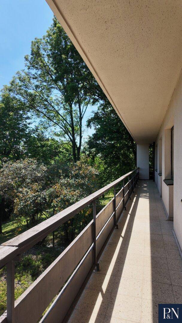Langer Balkon mit Geländer und Blick auf die umliegenden grünen Bäume.
