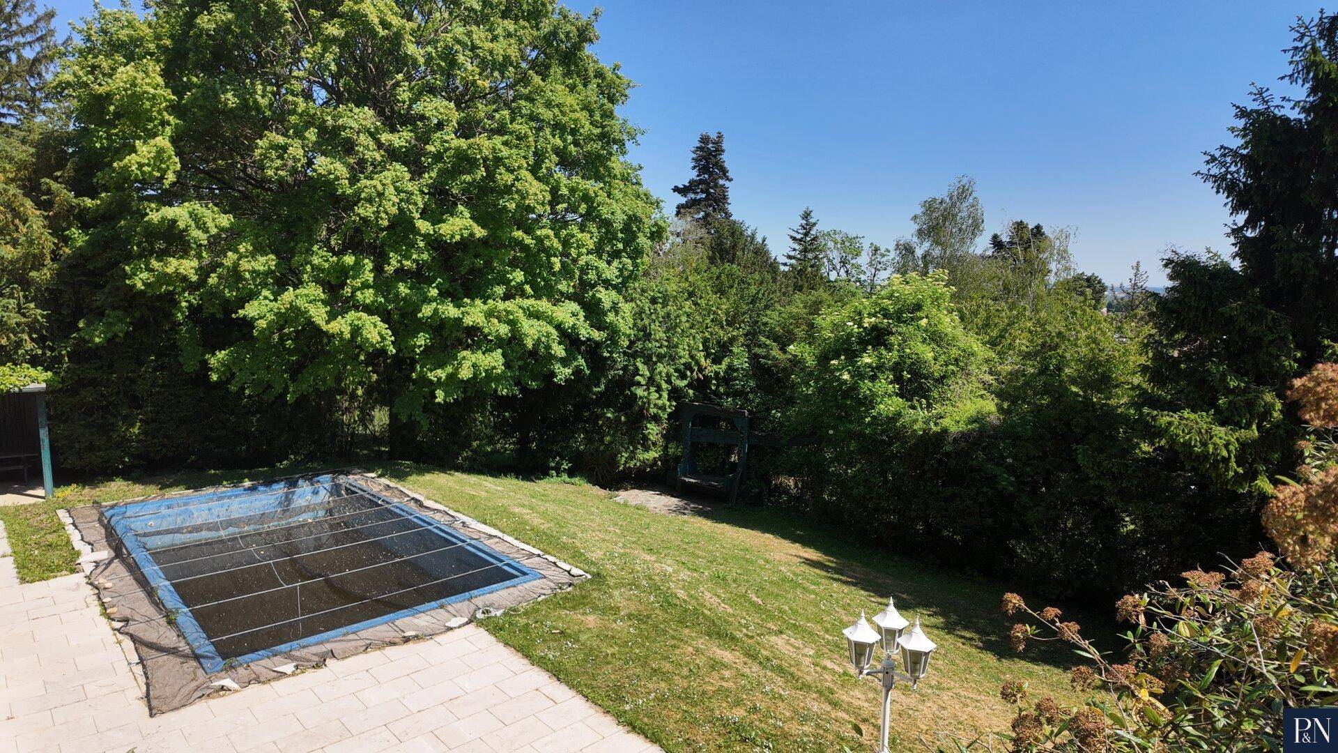 Großer Gartenbereich mit einem abgedeckten Swimmingpool und altem Baumbestand.