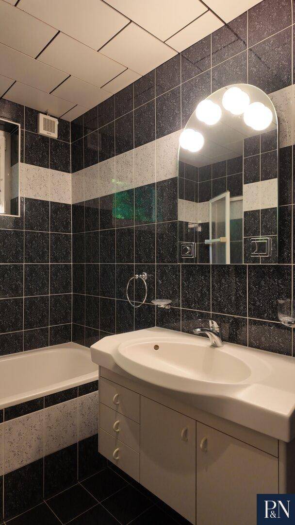 Badezimmer mit schwarz-weißen Fliesen, einem einzelnen Waschbecken und einer Badewanne.
