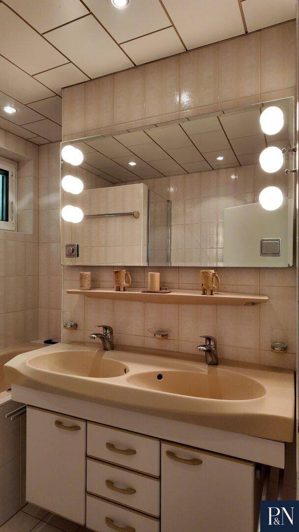 Badezimmer mit beigefarbenen Fliesen, einem Doppelwaschbecken und einem großen Spiegelschrank.