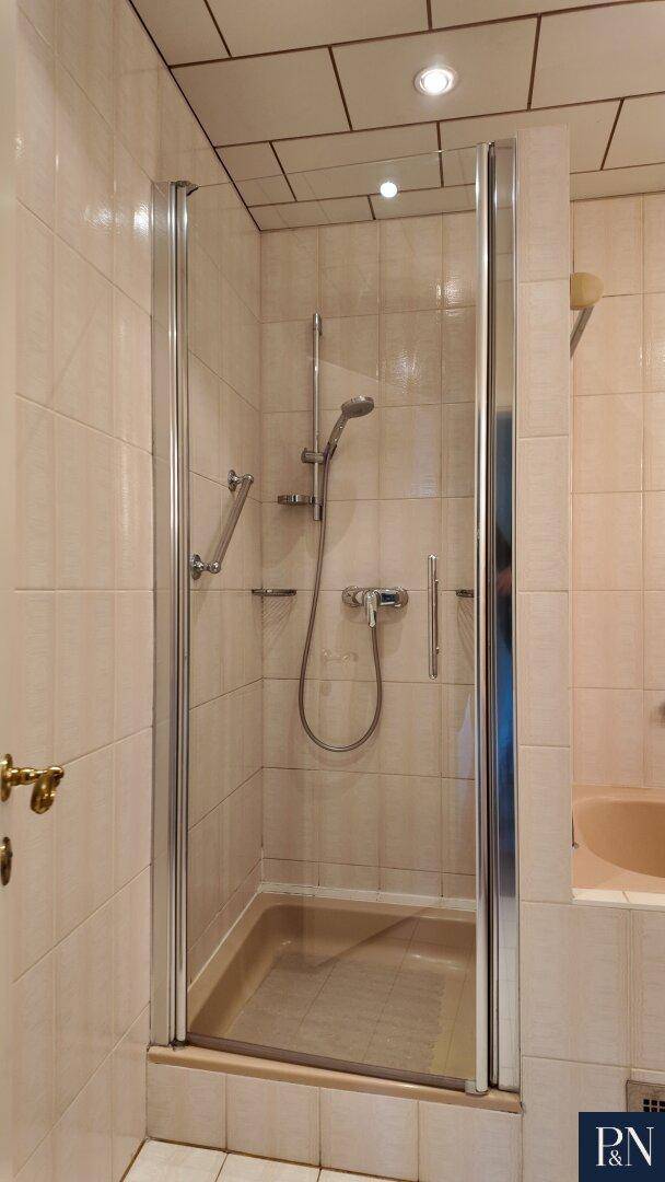 Duschkabine in einem Badezimmer mit hellen, beigefarbenen Fliesen und Duscharmatur.