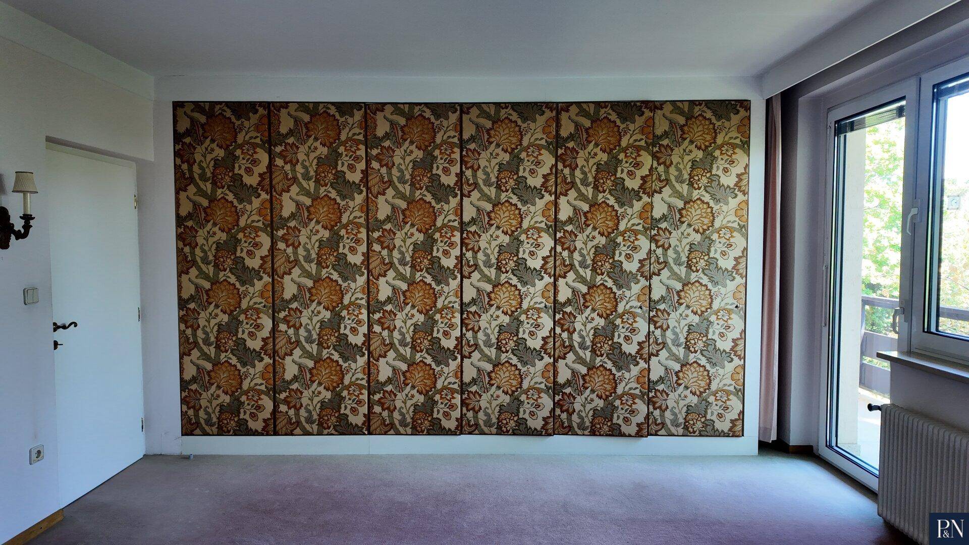 Schlafzimmer mit gemusterter Tapetenwand, Teppichboden und Fenster mit Zugang zum Balkon.