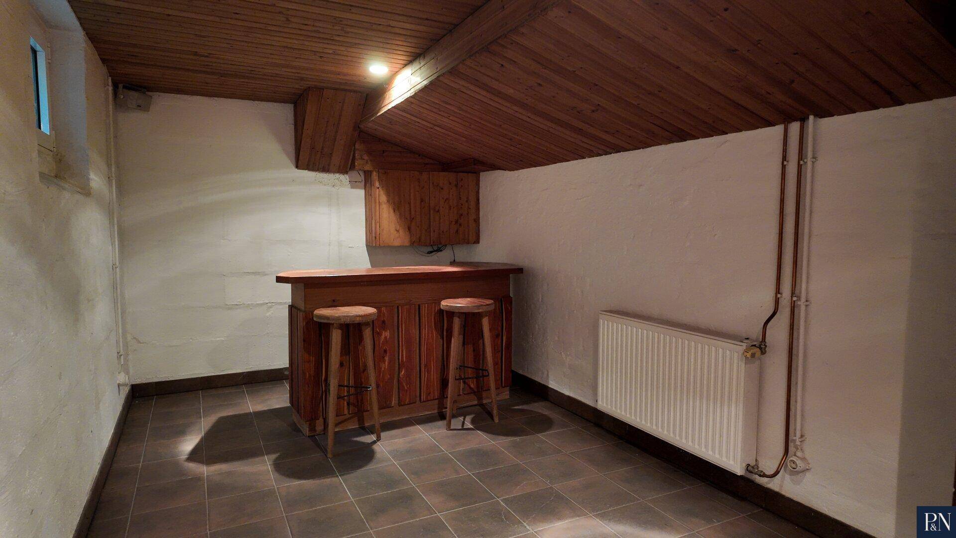 Kellerraum mit einer rustikalen Holzbar, Hockern und gefliestem Boden.