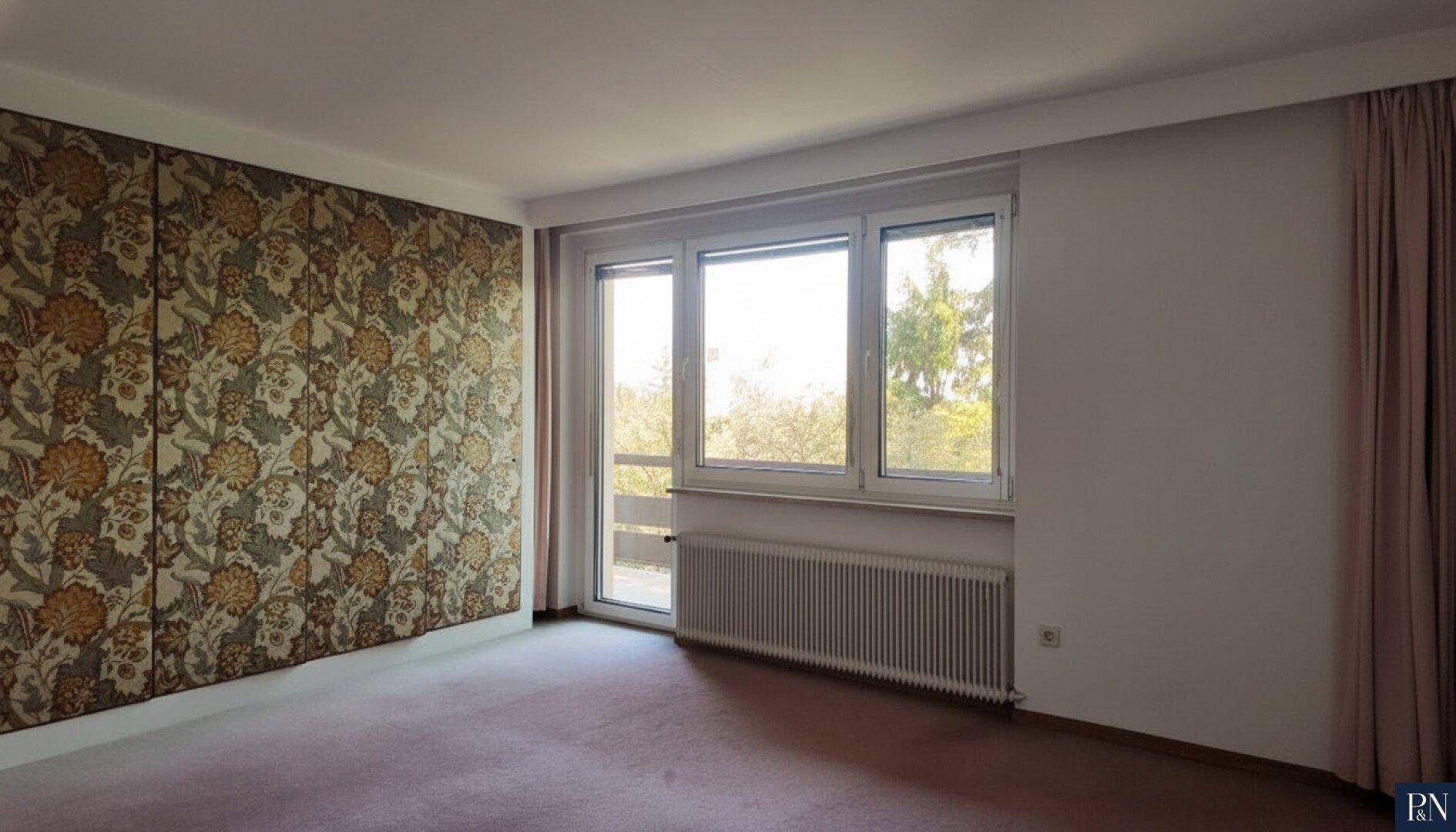 Helles Schlafzimmer mit auffälliger Tapetenwand, Teppichboden und großem Fenster.