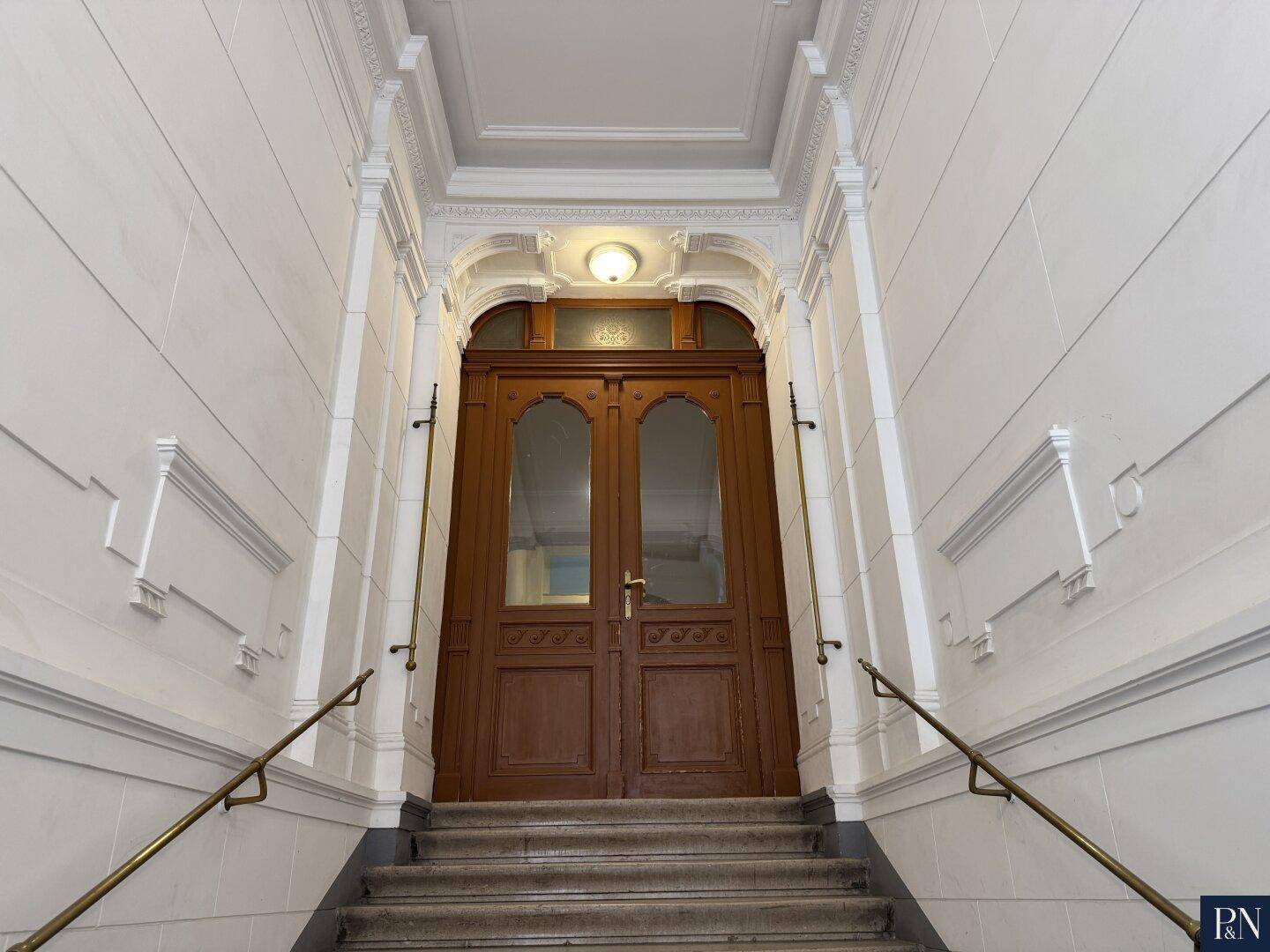 Repräsentativer Eingangsbereich eines Altbaus mit breiter Treppe und verzierten Türen.