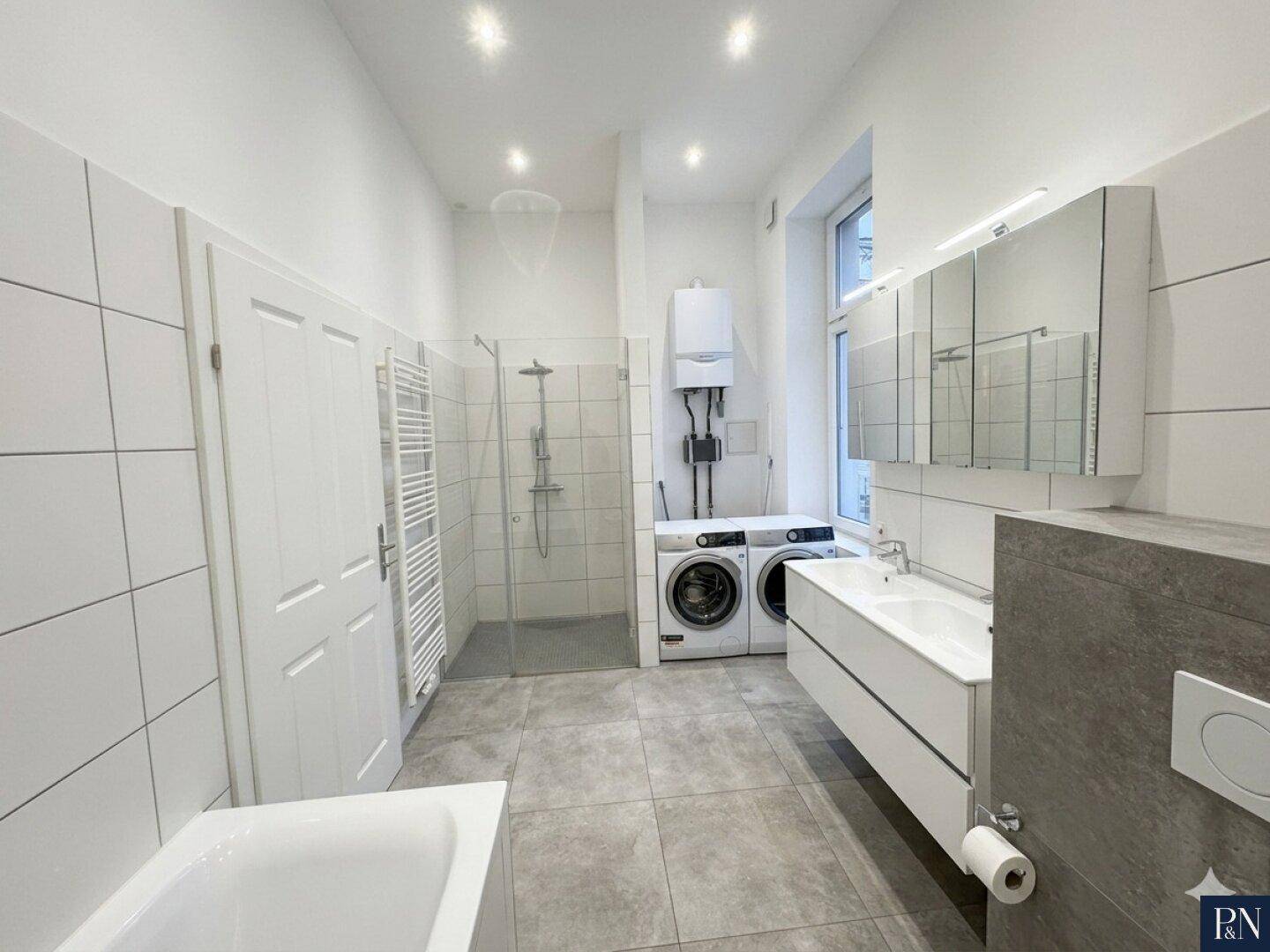 Großes Badezimmer mit Badewanne, Dusche, Doppelwaschbecken und Waschmaschinenanschluss.