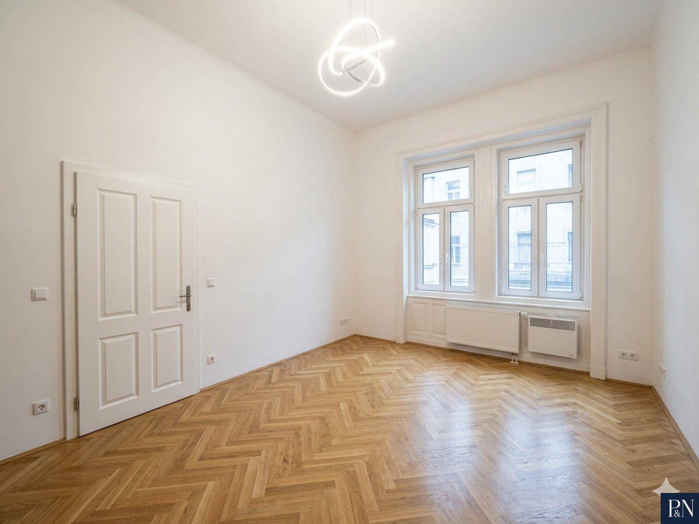 Geräumiges Zimmer mit klassischem Fischgrätparkett und hohen Decken, ideal für Wohn- oder Schlafbereich.